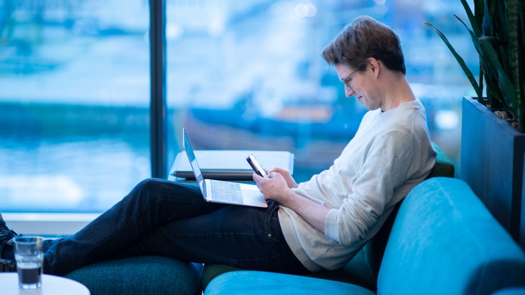 Person som sitter i en soffa med dator och mobiltelefon.