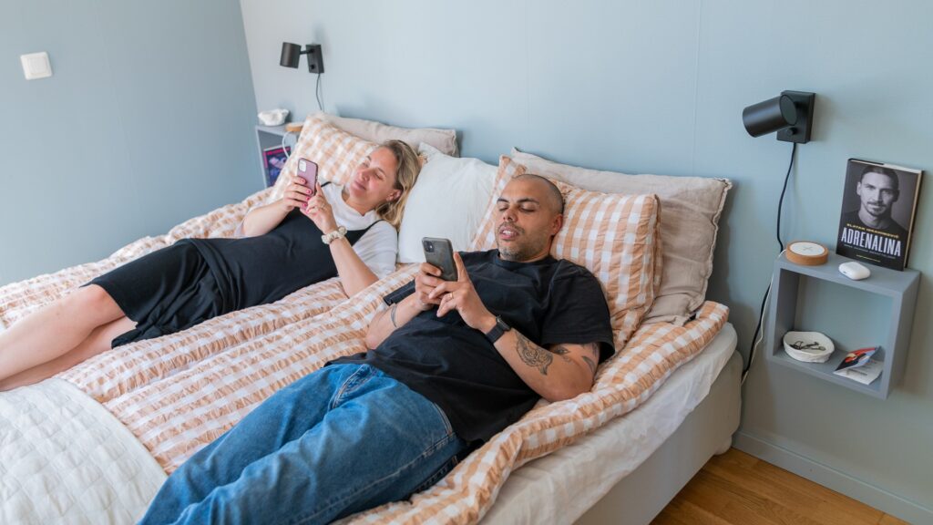 En man och en kvinna ligger i en säng och scrollar på varsin mobil.