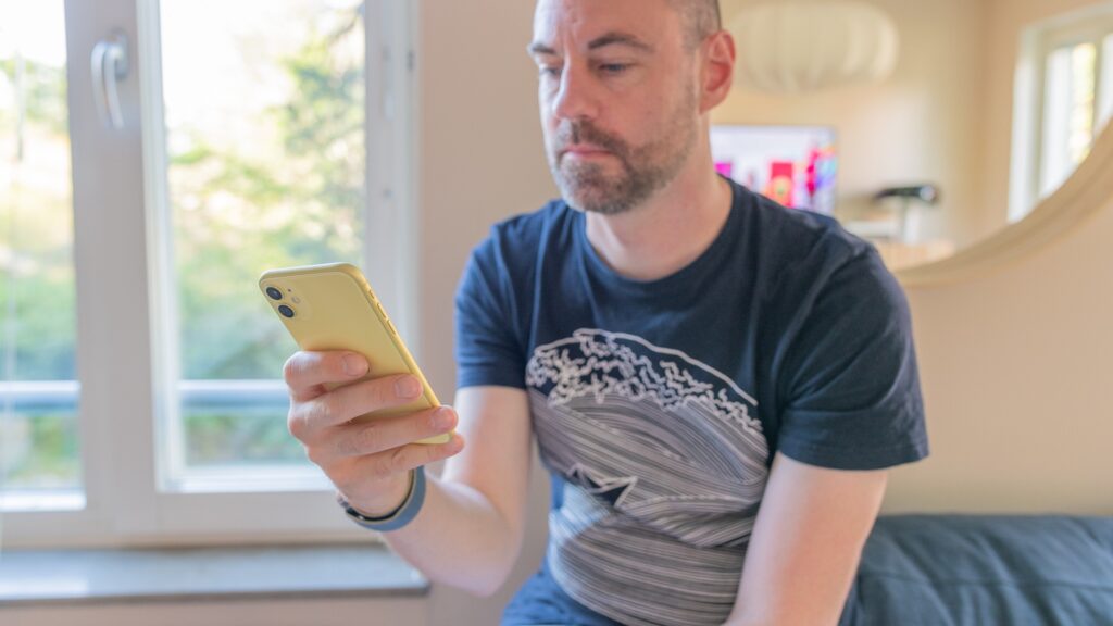 En man sitter med en mobil i handen.