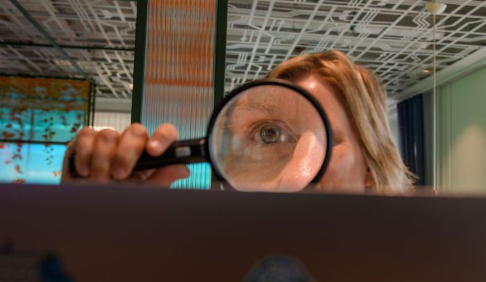 En kvinna håller ett förstoringsglas mot en datorskärm.