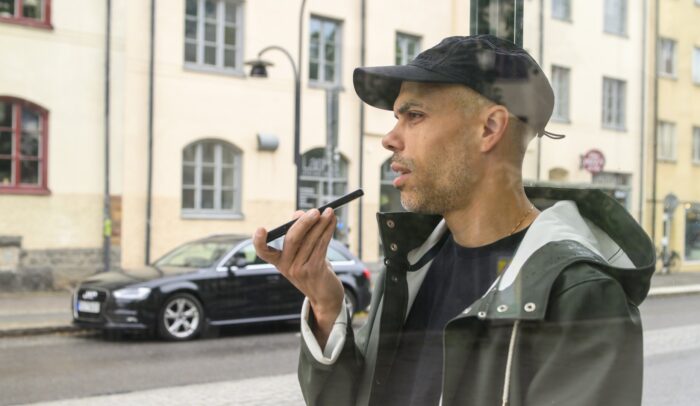 En man pratar i mobilen med högtalarläge i en busskur.
